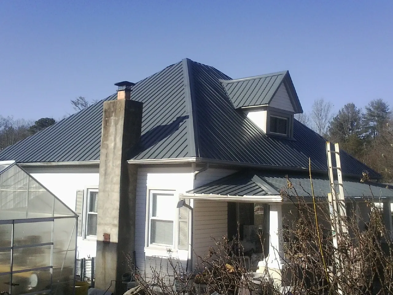 Dark blue standing seam metal roof on a white farmhouse with dormer — Slate & Tile Roof Repair by Roofing Brothers in Manchester