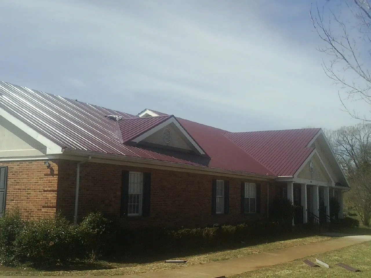 Red metal roof with gabled entries on a long brick building, from a Hail Damage Roof Repair job in Manchester