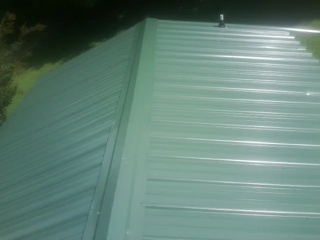 New green metal panels meeting at the ridge of a roof — Flat Roof Repair work by our crew in Manchester
