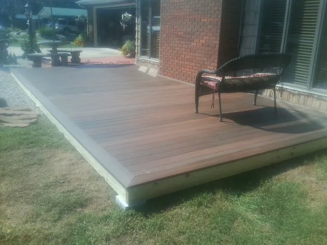 New wood deck and wicker chair beside a brick house in Manchester